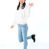 白背景で左手を挙げて挨拶する笑顔の女性のポートレートの写真