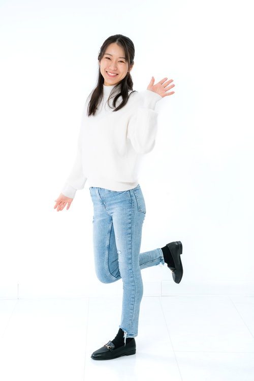 白背景で左手を挙げて挨拶する笑顔の女性のポートレート