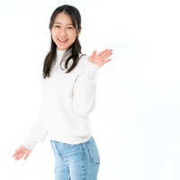 白いタートルネックを着て笑顔で手を挙げる女性の写真