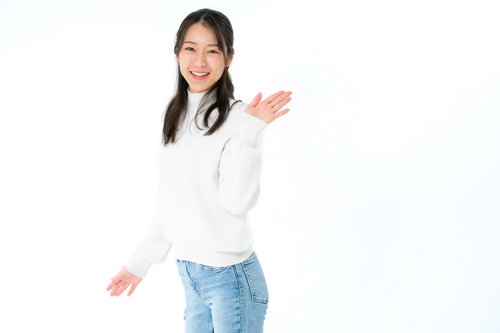 白いタートルネックを着て笑顔で手を挙げる女性