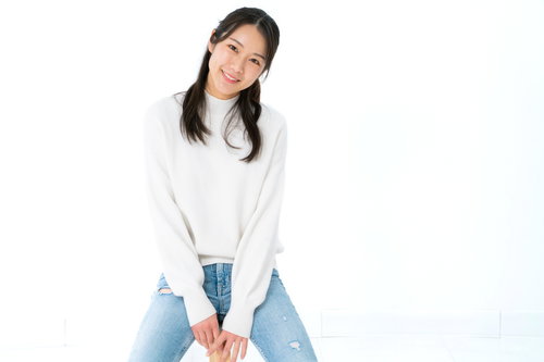 白背景で笑顔で腰を掛ける女性のポートレート