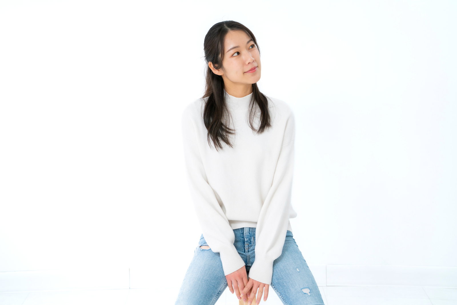 白い背景の前で椅子に座り、外方を向いている女性［モデル：SAKI］