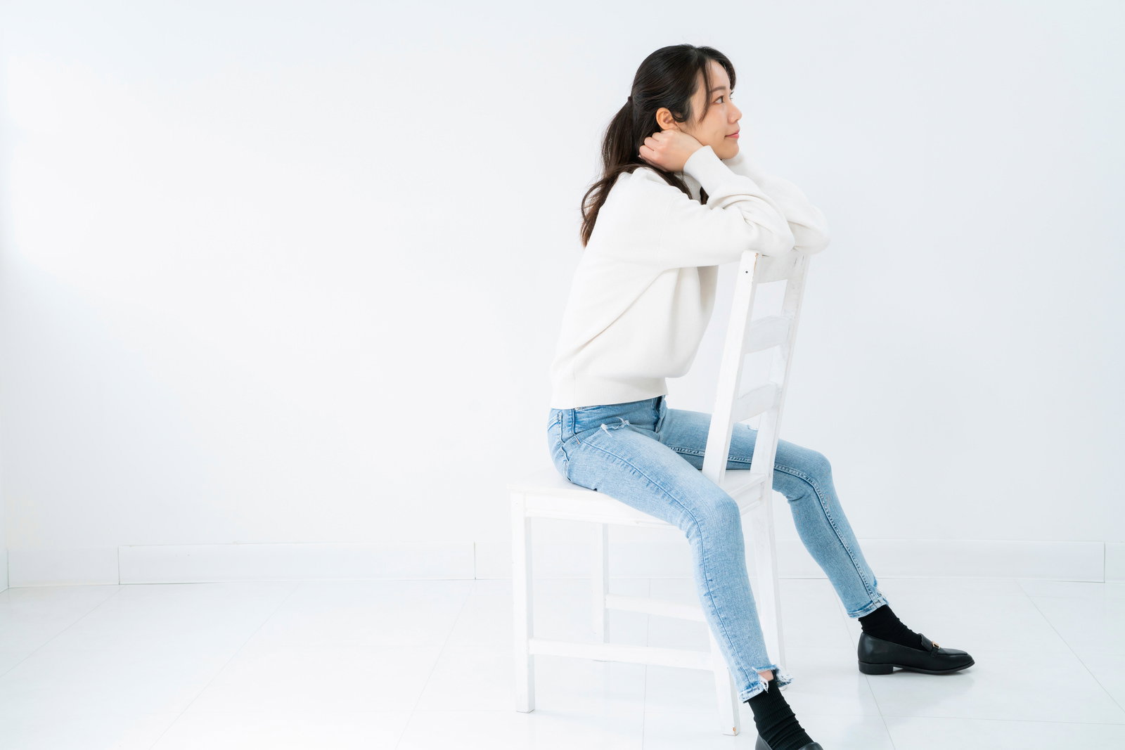 白背景で椅子に座りながら振り返る女性のポーズ［モデル：SAKI］