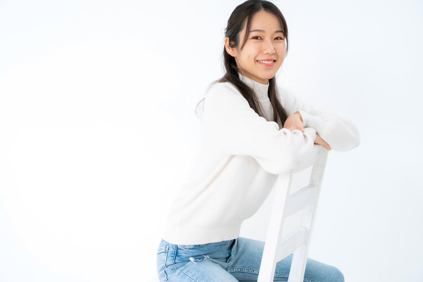 白いシャツとデニムを着た女性が腰掛けて笑顔でポーズを取る［モデル：SAKI］