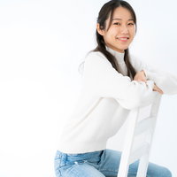 白いシャツにデニムを合わせて腰掛けて微笑む女性の写真