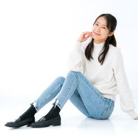 白背景で床に座り頬杖をつく女性のカジュアルポーズの写真