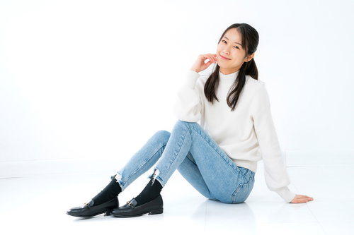 白背景で床に座り頬杖をつく女性のカジュアルポーズ