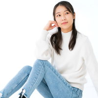 白い服を着て膝を立てて座り遠くを見つめる女性の写真