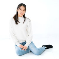 白背景で横座りするニット姿の女性のポートレートの写真