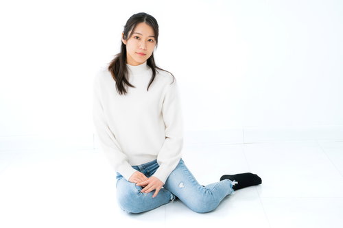 白背景で横座りするニット姿の女性のポートレート