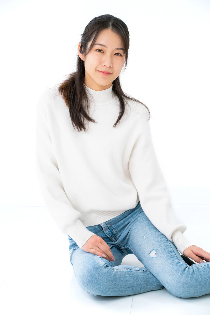 白いニットとデニムを着た女性が横座りして微笑んでいる［モデル：SAKI］