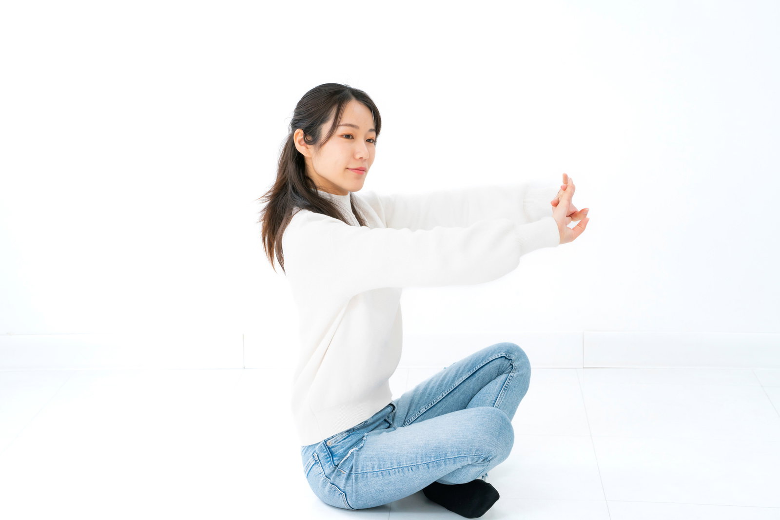 床に座って両手を上に伸ばしストレッチをする白い服の女性［モデル：SAKI］