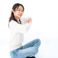 白背景で腰を下ろして伸びをしようとする女性の写真