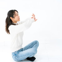 白いシャツとジーンズであぐら座りでストレッチする女性の写真