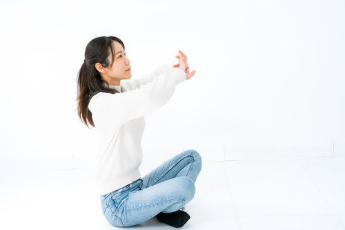 白いシャツとジーンズであぐら座りでストレッチする女性