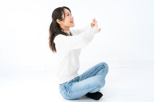 白背景であぐら座りで柔軟体操をする女性のストレッチポーズ