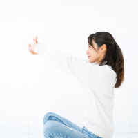 白背景であぐら座りで片腕を前方に伸ばしてストレッチする女性の写真