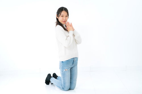 白いセーターを着て両手を合わせて膝立ちする黒髪女性