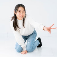 白背景で膝立ちしてピースする笑顔の女性ポートレートの写真