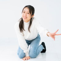 白背景で膝立ちしながらピースサインを送る微笑む女性の写真