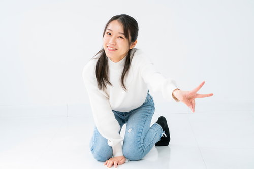 白背景で膝立ちしながらピースサインを送る微笑む女性