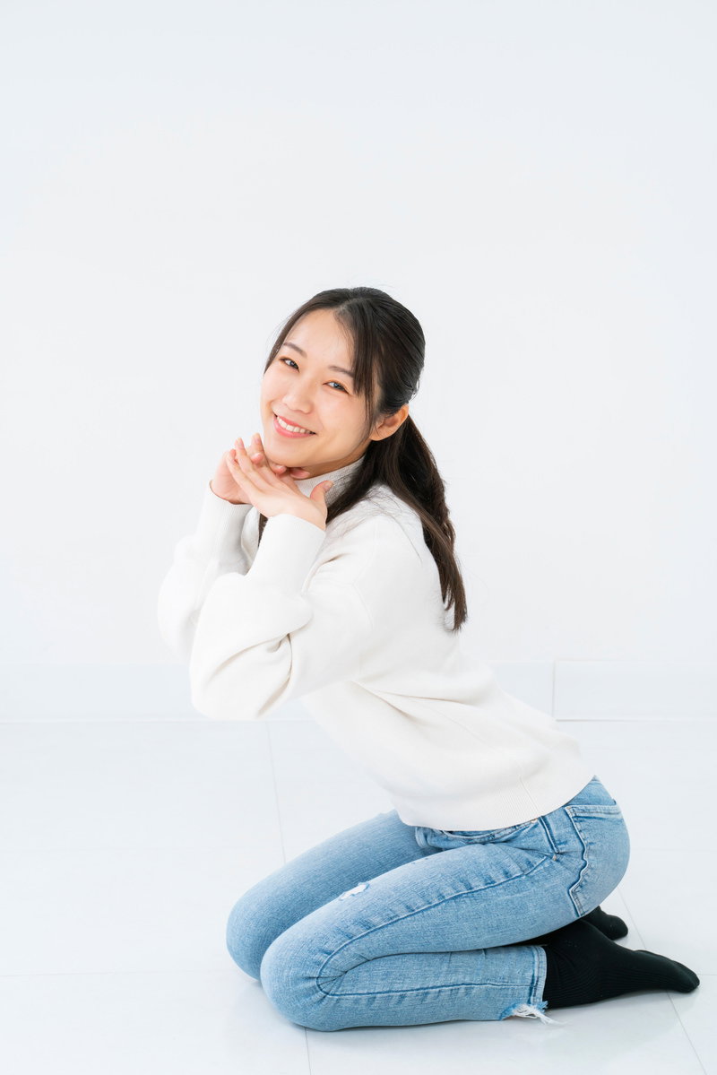 白背景で正座し顎をのせてニッコリ笑う女性［モデル：SAKI］