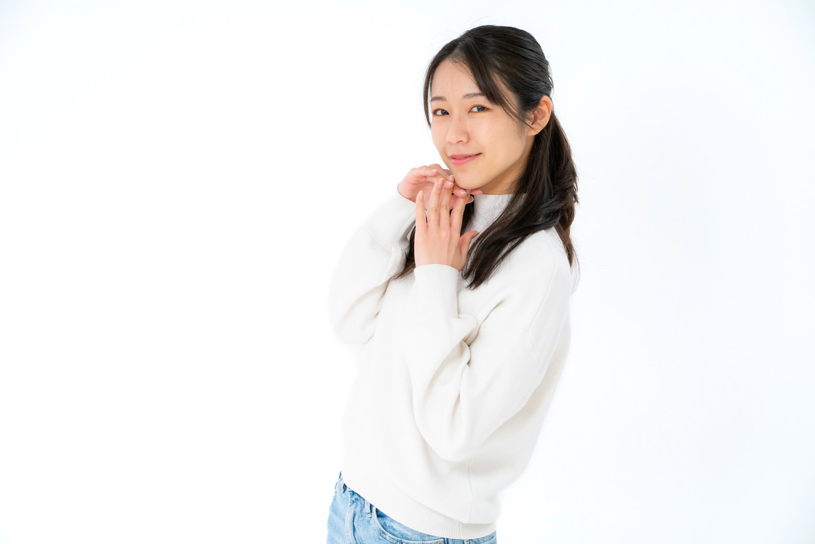 白いセーターを着て、指先を顎に向けて微笑む女性［モデル：SAKI］