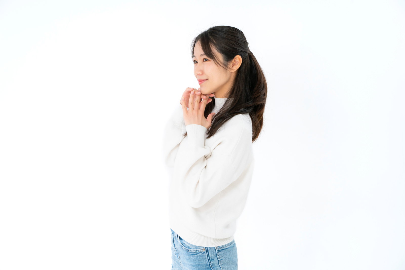 白いニットと青いデニムを着た女性が右向きで笑みを浮かべている横顔［モデル：SAKI］