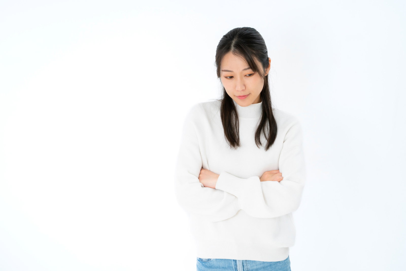 白背景で腕組みして下を向き思い悩む女性［モデル：SAKI］