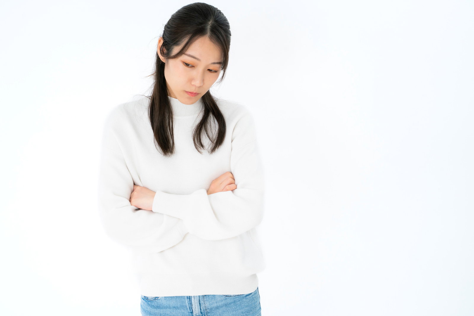 白いセーターを着た女性が腕を組んで下を向いている［モデル：SAKI］