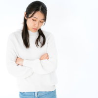 腕を組んで下を向く女性の悩み・不安・ストレス表現ポーズの写真