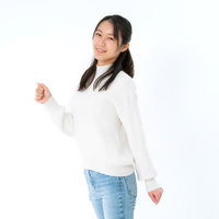 白背景で笑顔で踏み出す女性、白いセーターとジーンズ姿の写真