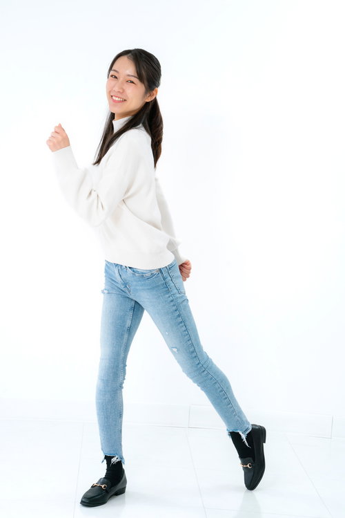 笑顔で歩き出す女性のポーズ、白シャツとデニムパンツのカジュアルスタイル