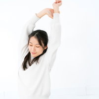 白背景で手を上に伸ばしてストレッチする女性の写真