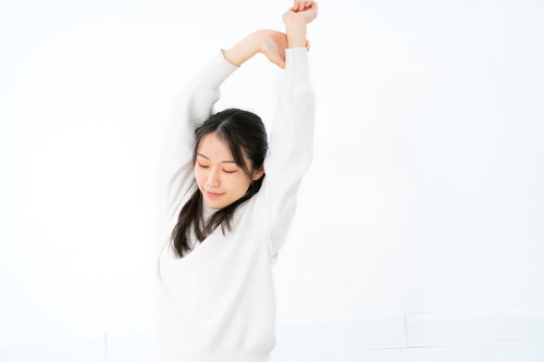 白背景で手を上に伸ばしてストレッチする女性