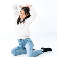 横座りしながら両腕を上げて伸びる女性のストレッチポーズの写真