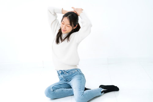 横座りしながら両腕を上げて伸びる女性のストレッチポーズ