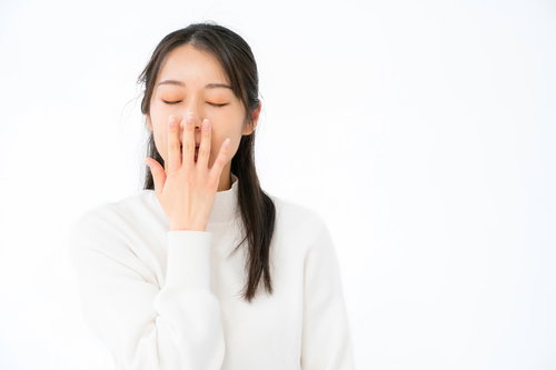 退屈であくびが止まらない白い長袖姿の女性