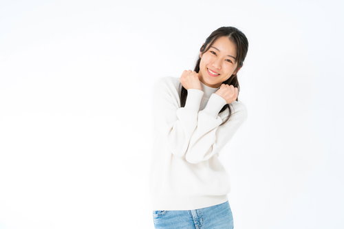 白いニットを着て笑顔でぶりっ子ポーズをする女性