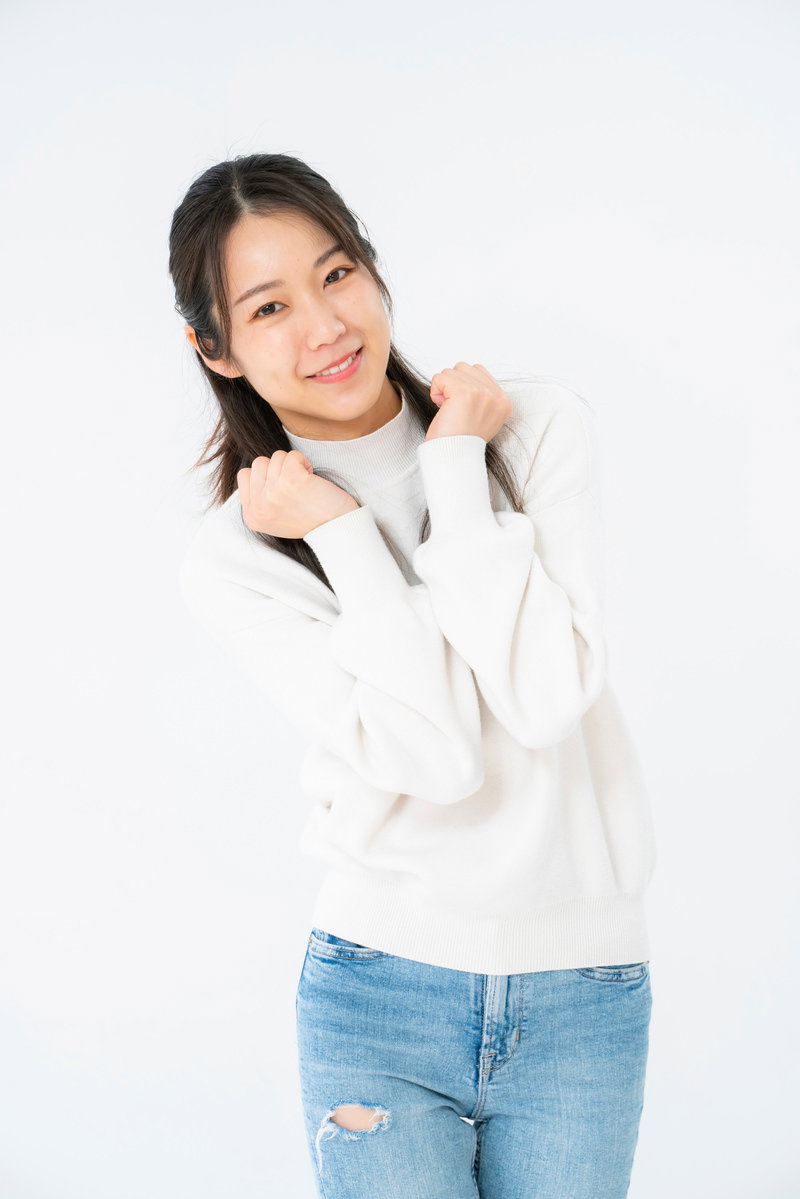 白いニットを着た女性が体を傾けてぶりっ子ポーズをして笑っている［モデル：SAKI］