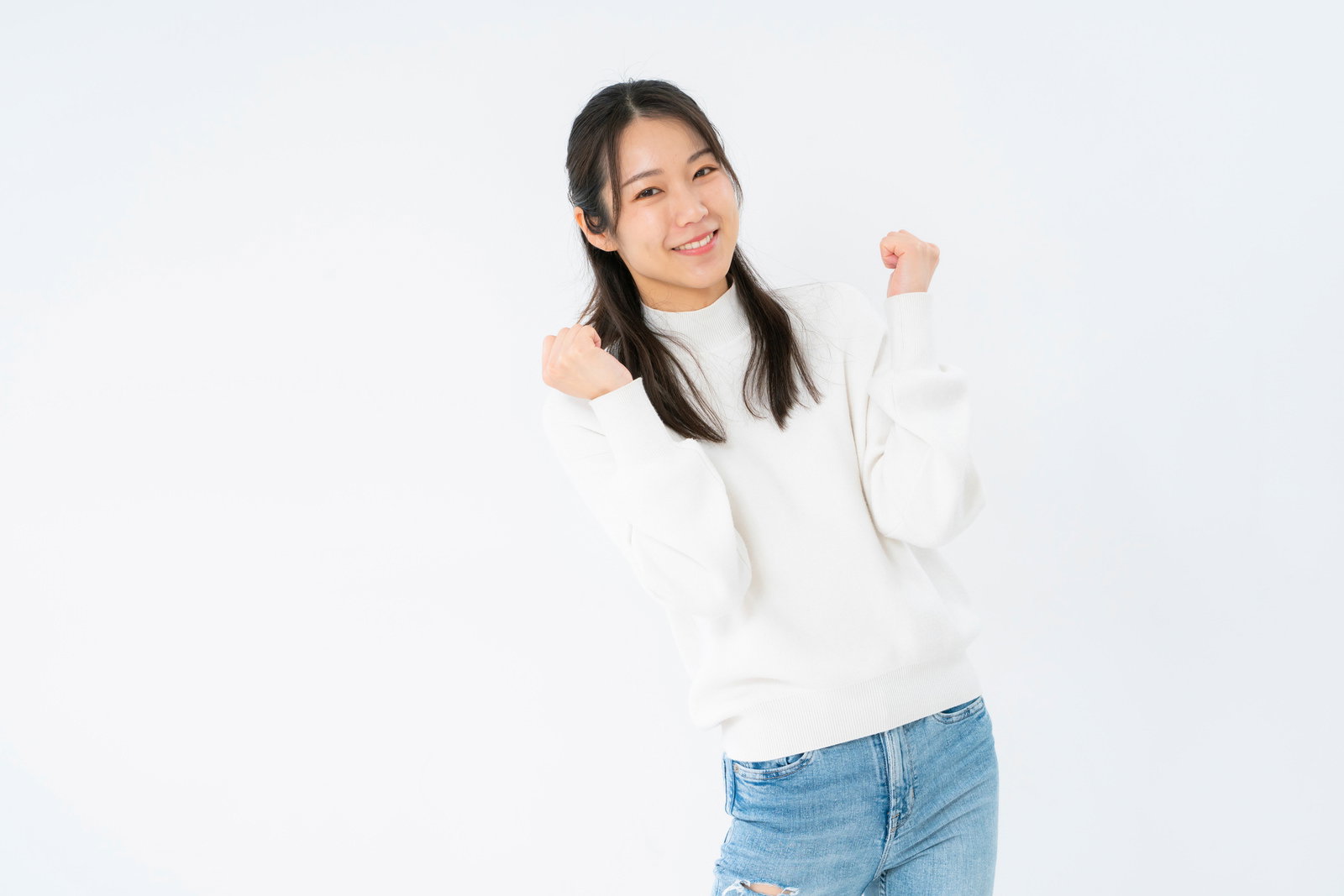 白いセーターを着た女性が控えめにガッツポーズをして笑っている［モデル：SAKI］