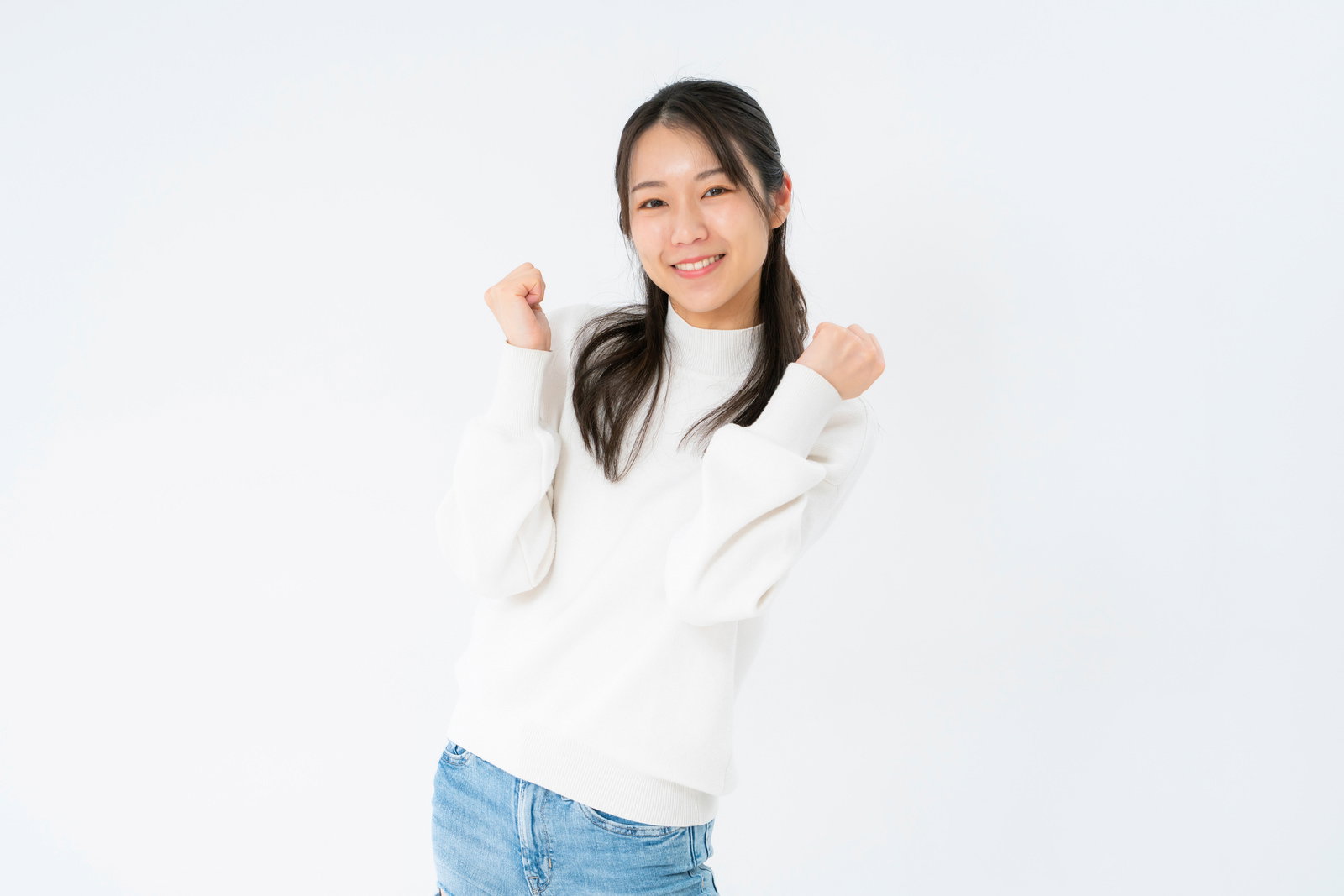 A woman in a white sweater and denim pants raising her hands in a celebratory pose and smiling