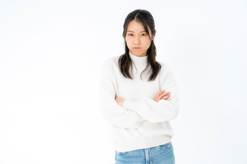 白いタートルネックで腕組みする不機嫌な表情の女性