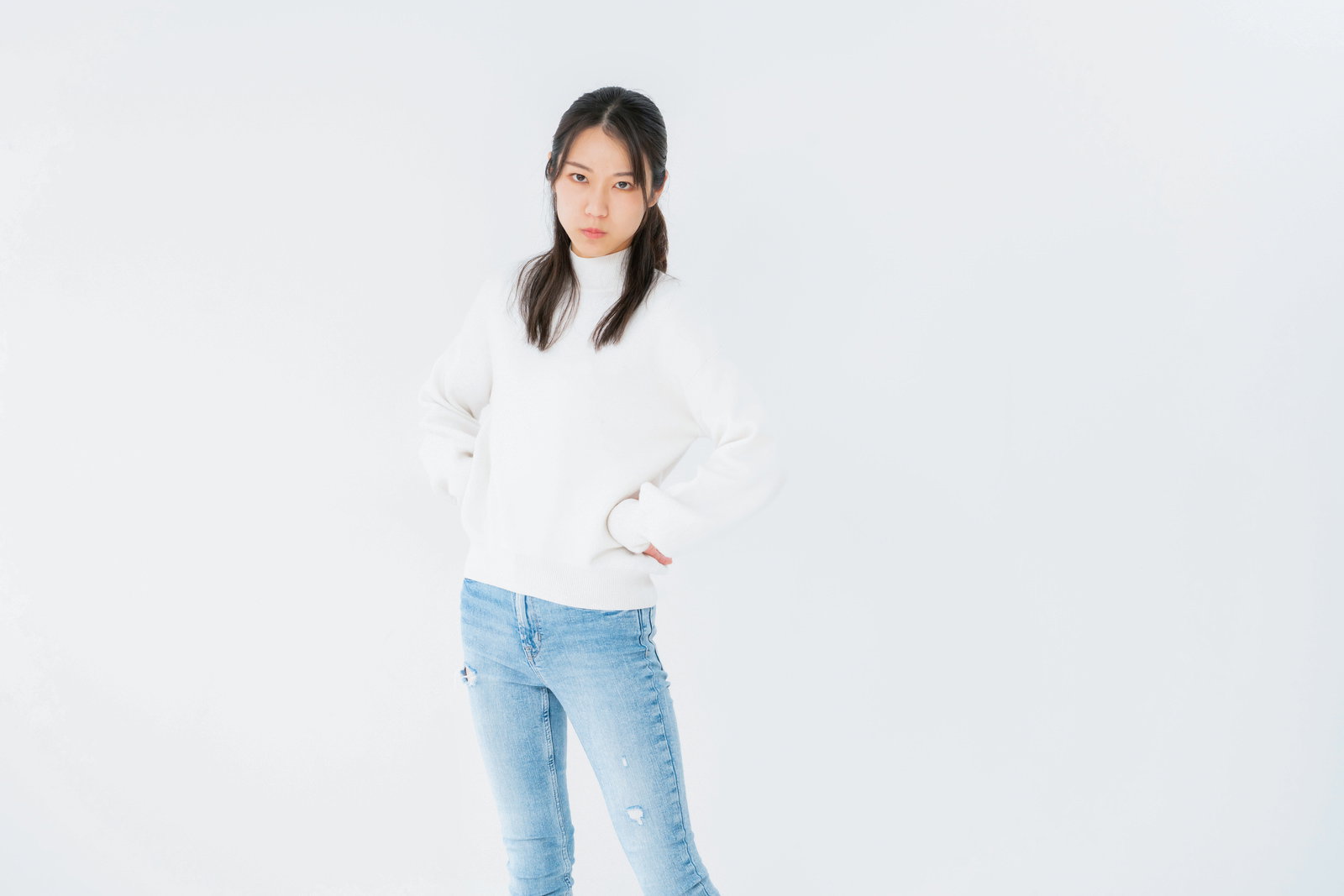 腰に手を当てて睨みつける女性が、不機嫌な表情で正面を向いている［モデル：SAKI］