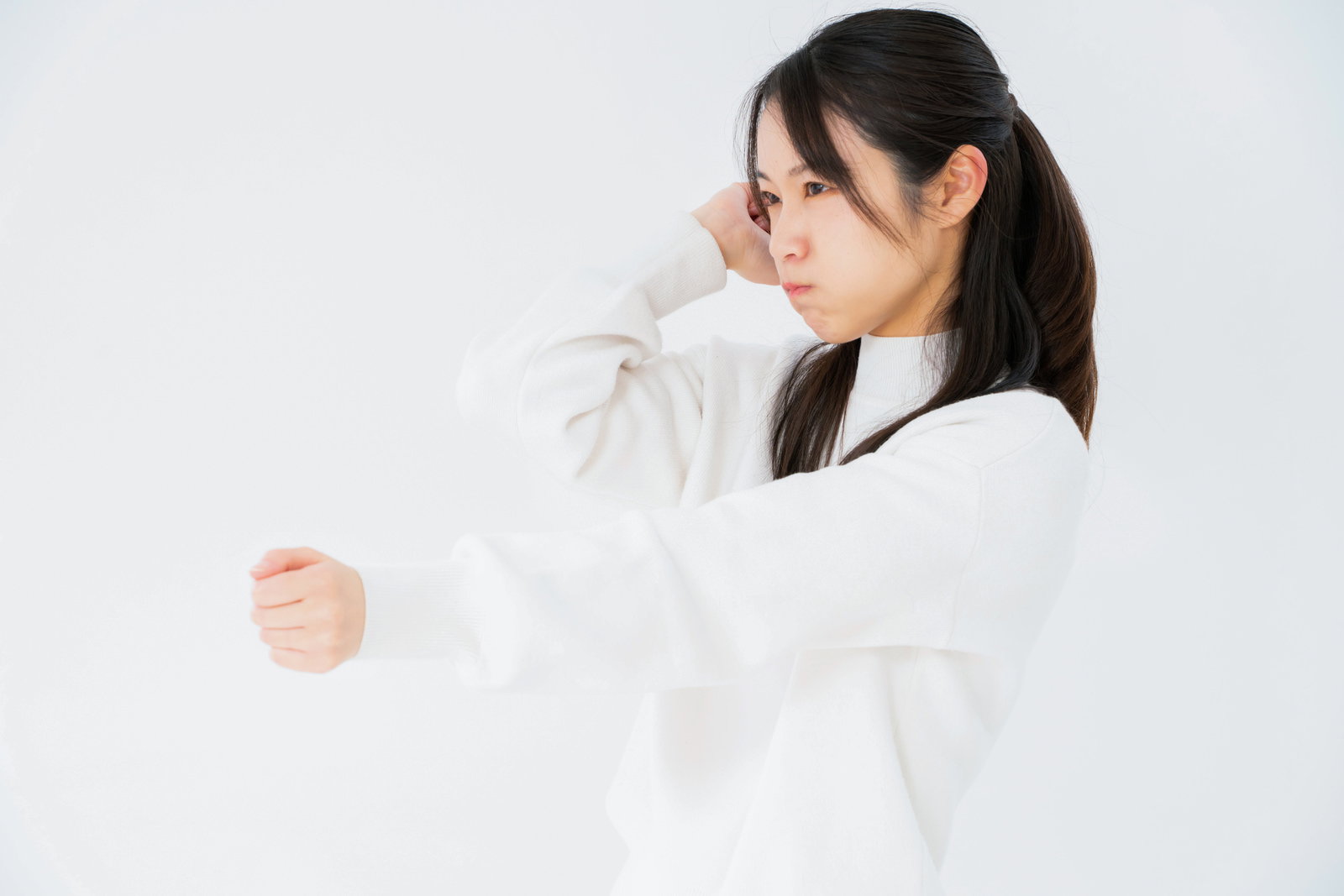白いシャツを着た女性が怒った表情で拳を握り殴ろうとしている［モデル：SAKI］