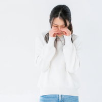 目を押さえてめそめそする白いニットの女性のポーズの写真