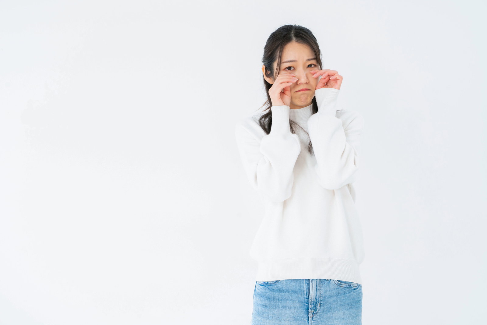 白いニット姿で両手で目をこすりながら泣く女性［モデル：SAKI］