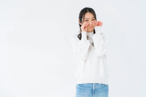 白いニットを着てウソ泣きする女性のポーズ