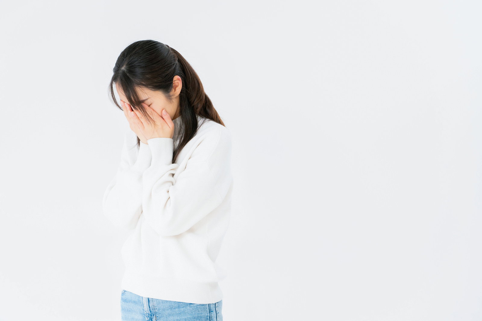 白いセーターを着た女性が両手で顔を覆い泣いている姿［モデル：SAKI］