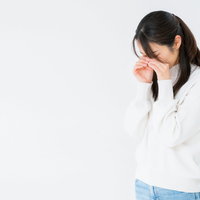 白背景の前で顔を手で覆いながらめそめそする女性の写真